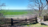 Holzzaun mit offenem Tor vor einer weiten grünen Marschlandschaft unter blauem Himmel
