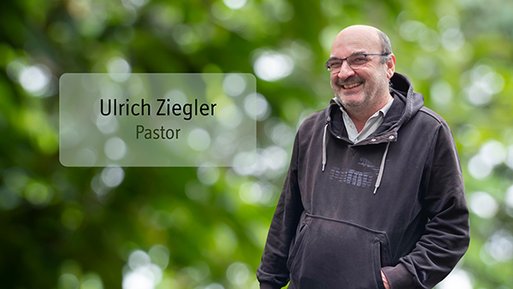 Ulrich Ziegler Mann mit Brille und Kapuzenpullover steht lächelnd vor unscharf grünem Hintergrund.