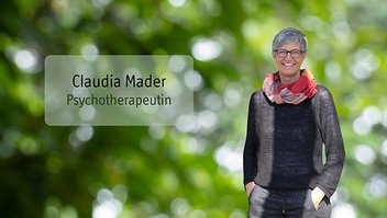 Claudia Mader Frau mit kurzen grauen Haaren, Brille und buntem Schal steht lächelnd vor unscharf grünem Hintergrund mit Textfeld 'Claudia Mader Psychotherapeutin'.