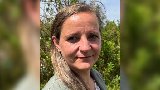 Kerstin Gottfried Frau mit langem, glattem Haar und grünem Oberteil vor grünem, unscharfem Hintergrund.