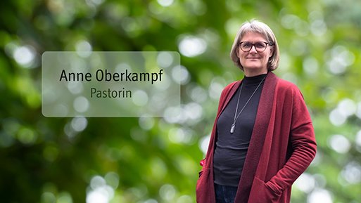 Anne Oberkampf Frau mit Brille und grauen Haaren trägt schwarzen Pullover und roten Cardigan vor unscharf grünem Hintergrund.